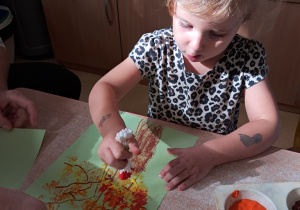 Zosia stempluje liście w czasie wykonywania pracy plastycznej