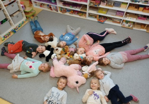 Dzieci leżą na podłodze obok swoich przytulanek