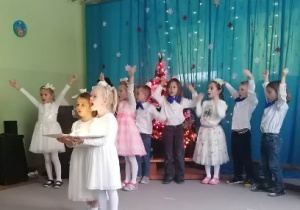 Dzieci śpiewają piosenkę podczas występu jasełkowego, dwie dziewczynki stoją na środku trzymając rekwizyty