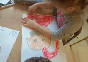 Dziewczynka przy stoliku maluje rysunek Świętego Mikołaja przy użyciu pasteli olejnych.