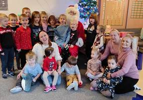 Grupa dzieci wraz z wychowawcami pozuje do zdjęcia ze Świętym Mikołajem.
