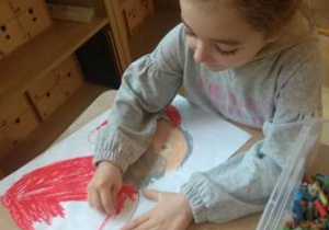 Dziewczynka przy stoliku koloruje narysowany przez nią portret Świętego Mikołaja.