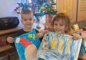 Dwaj chłopcy trzymają swoje prace i pokazują rysunki Świętego Mikołaja.