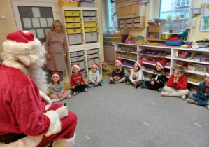 Święty Mikołaj siedzi na krześle, dzieci siedzą na dywanie