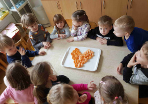 Dzieci siedzą przy stole, na którym leży talerz z mandarynkami ułożonymi w kształcie serca