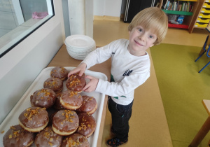 Chłopiec degustuje pączki.