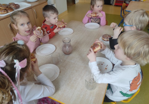 Dzieci przy wspólnym stole jedzą pączki.