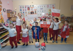 Zdjęcie grupowe, na którym widać dzieci z flagami, szalikami, piłkami i koszulkami piłkarskimi