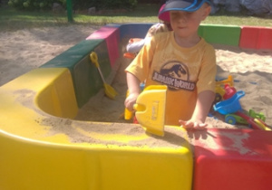 Chłopiec konstruuje budowle z piasku w piaskownicy w ogrodzie