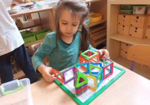 Dziewczynka konstruuje budowle z klocków magnetycznych