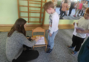 Dzieci stoją czekają na swoją kolej, chłopiec podaje pani książeczkę