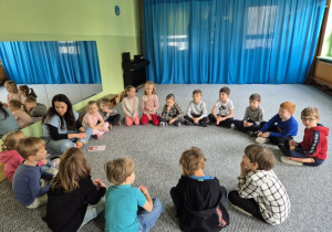 Dzieci siedzą w kręgu i słuchają prowadzącej zajęcia
