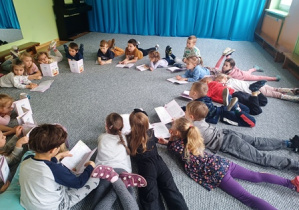 Dzieci leżą na dywanie i oglądają książeczki edukacyjne