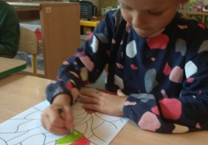 Dziewczynka koloruje mozaikę stanowiącą kształt drzewa.