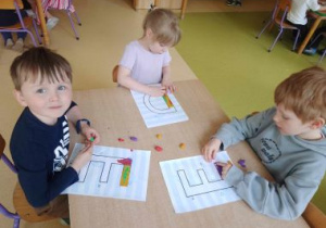 Dzieci siedzą przy stoliku i wylepiają plasteliną wybraną przez siebie literkę