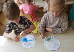 Dzieci stemplują model Ziemi patyczkami kosmetycznymi umoczonymi w farbie.