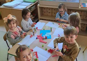 Dzieci przy stoliku w czasie wykonywania pracy plastycznej przedstawiającej flagę Polski