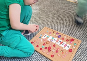 Julia układa kamyczki wokół napisu "Polska"