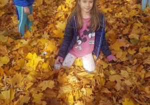 Dziewczynka siedzi na stercie jesiennych liści