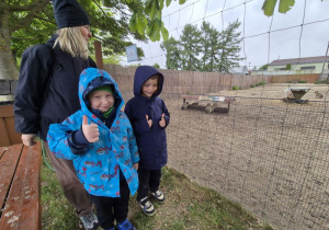 Chłopcy stoją przed zagrodą obok pani i pozują do zdjęcia