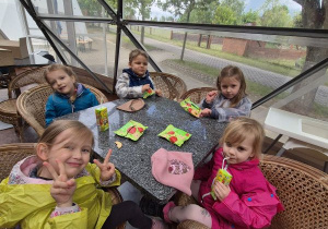 Dzieci siedzą przy stoliku, piją soczki i jedzą suszone jabłka