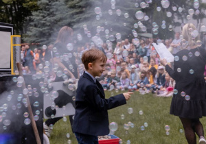 Chłopiec stoi przed bańkami mydlanymi unoszącymi się w powietrzu