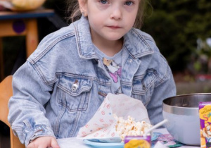 Dziewczynka siedzi przy stoliku i je popcorn
