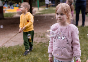 Dziewczynka w różowej bluzie stoi i patrzy przed siebie