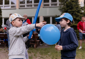 Dwóch chłopców z lizakami w buzi stoi z niebieskimi balonami w dłoniach