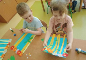 Dziewczynka z chłopcem przyklejają paski na swojej pracy