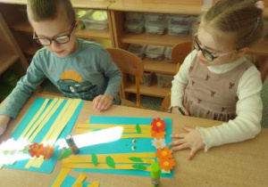 Dzieci przyklejają żółte paski na niebieskiej kartce