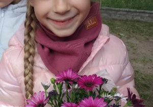 Dziewczynka pozuje do zdjęcia i trzyma w dłoniach sadzonkę z kwiatami