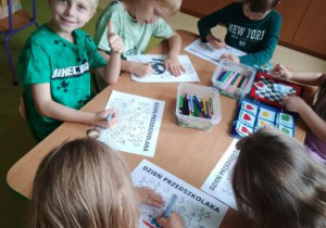 Dzieci siedzą przy stoliku i kolorują obrazki