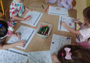 Dzieci siedzą przy stoliku i kolorują obrazki