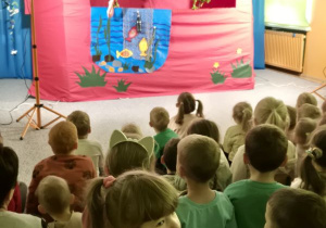 Dzieci oglądają przedstawienie siedząc na widowni, na scenie występują dwie żabki