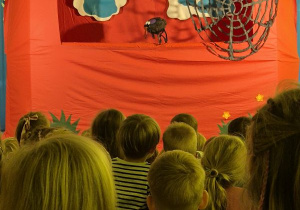 Dzieci oglądają przedstawienie siedząc na widowni, na scenie pająk i pajęczynka