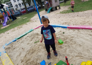 Chłopiec stoi w piaskownicy.