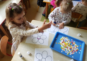 Dziewczynki wyklejają kolorowymi kropkami kontur obrazka