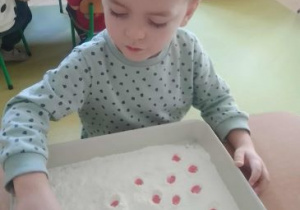 Chłopiec paluszkiem tworzy kropki w rozsypanej na tacy mące