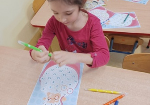 Dziewczynka siedzi przy stoliku i rysuje mazakami