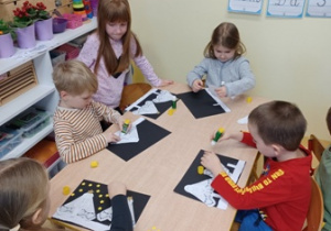 Dzieci w trakcie pracy plastycznej - przyklejania choinek z serwetek i gwiazd z papieru