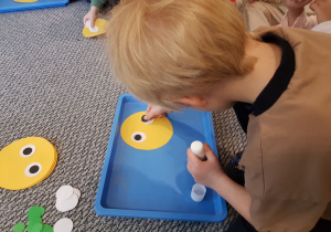 Chłopiec przykleja oczy z kolorowych kół