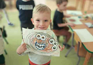 Chłopiec trzyma w dłoniach wykonaną przez siebie pracę plastyczną pt. "Potworek pełen emocji"