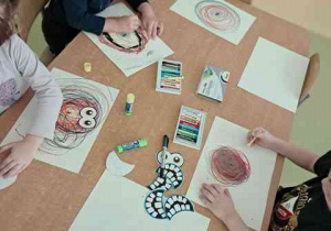 Dzieci w czasie działań manualnych przy stoliku - rysują okręgi przy użyciu pasteli