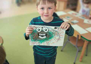 Chłopiec prezentuje wykonaną przez siebie pracę plastyczną pt. "Potworek pełen emocji"