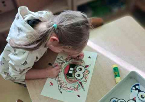 Wiktoria podpisuje przy użyciu mazaka swoją pracę plastyczną pt. "Potworek pełen emocji"