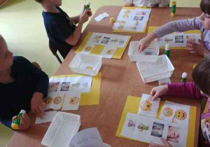 Dzieci przy stoliku w czasie wykonywania karty pracy przedstawiającej ilustracje różnych emocji