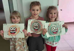 Dziewczynki pozują do zdjęcia z wykonanymi przez siebie pracami plastycznymi pt. "Potworek pełen emocji"