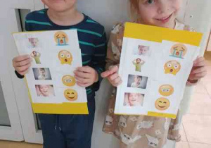 Bruno i Zosia pozują do zdjęcia z kartami pracy dotyczącymi emocji