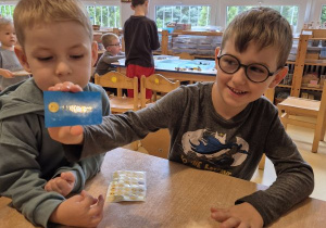 Chłopiec pozuje do zdjęcia ze swoją wizytówką, obok stoi drugi chłopiec